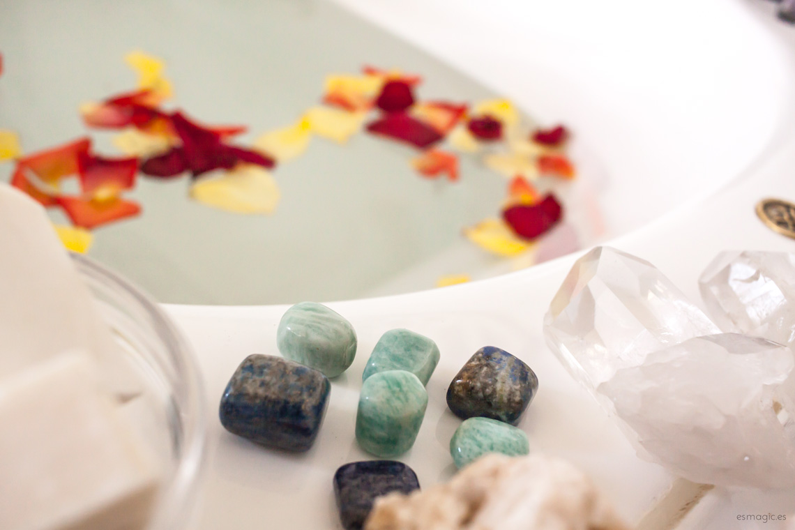 imagen de un baño con minerales de amazonita, lapislázuli, jabón natural y pétalos flotando en el agua de la bañera